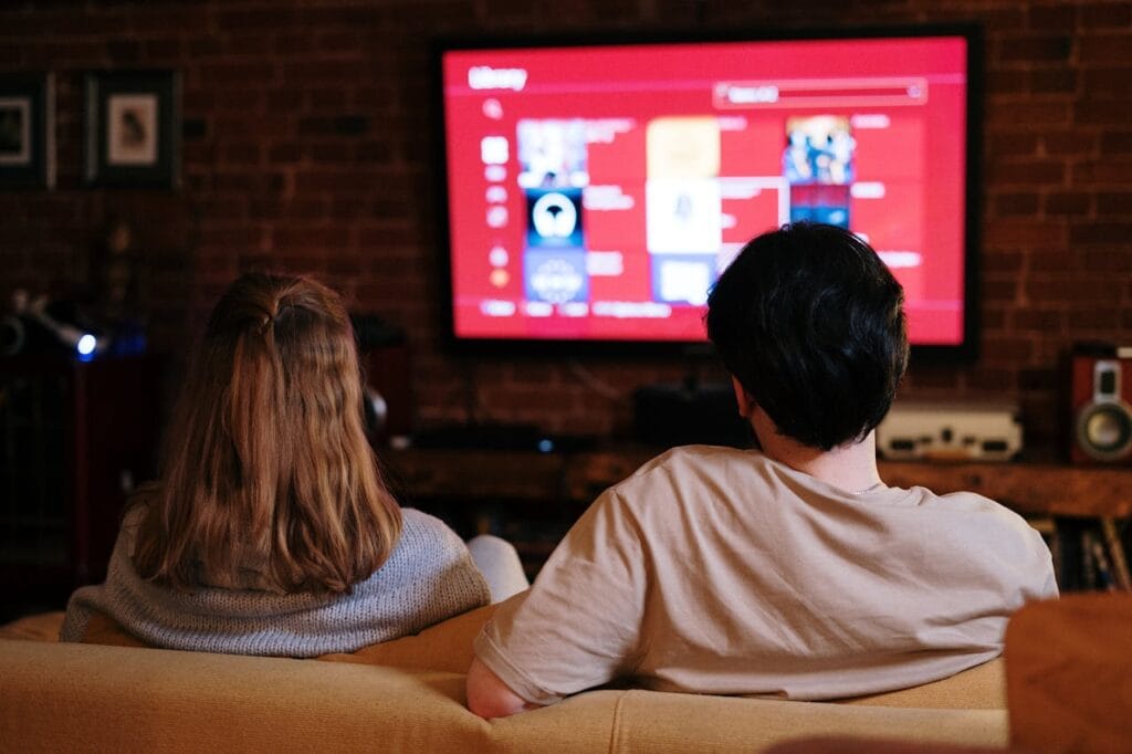 Momak i devojka sede na kauču i gledaju TV