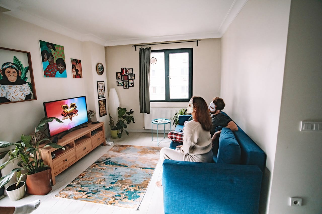Momak i devojka sede na plavom kauču i gledaju televiziju